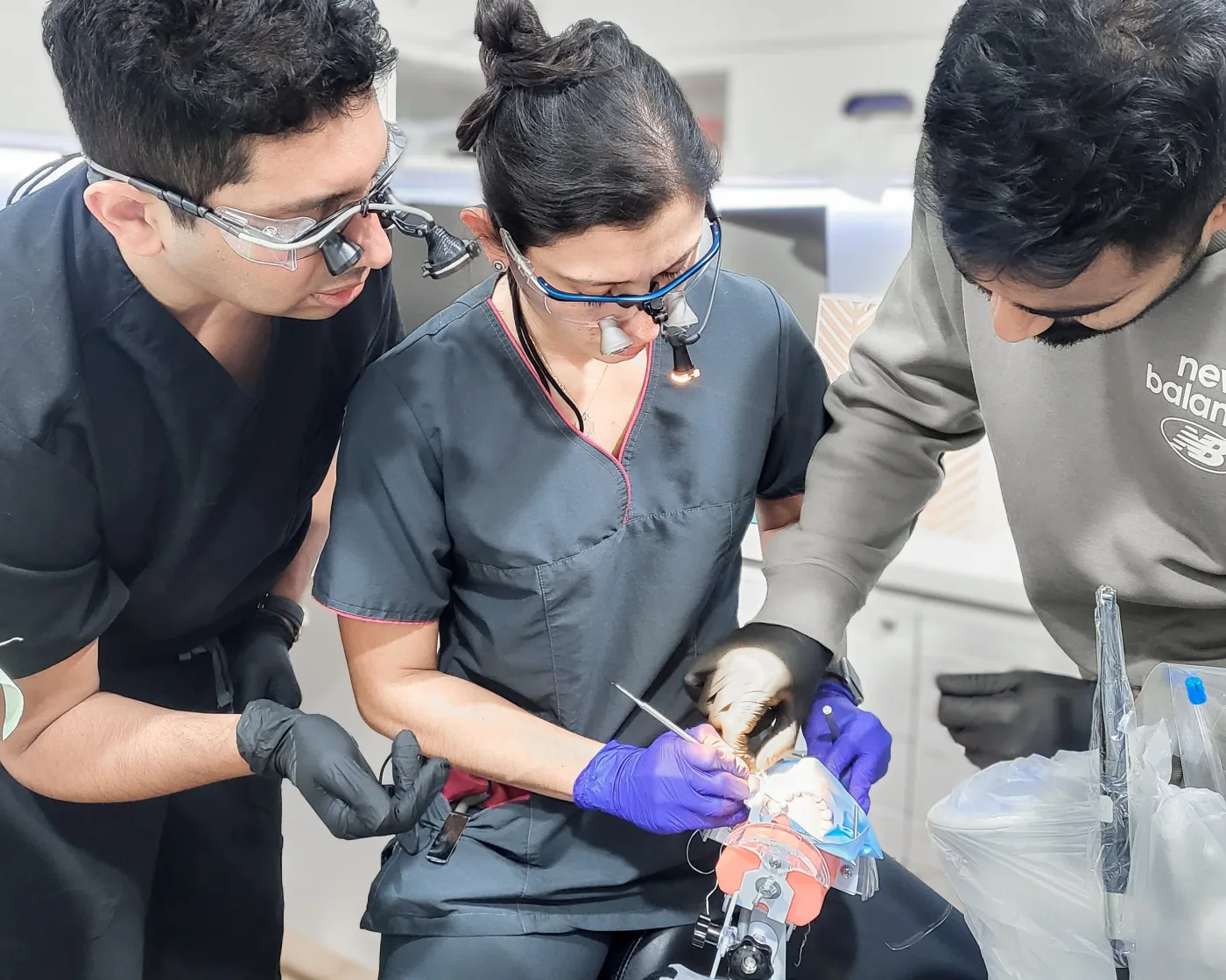 Three dentists in loupes working together on a typodont during a hands-on clinical session