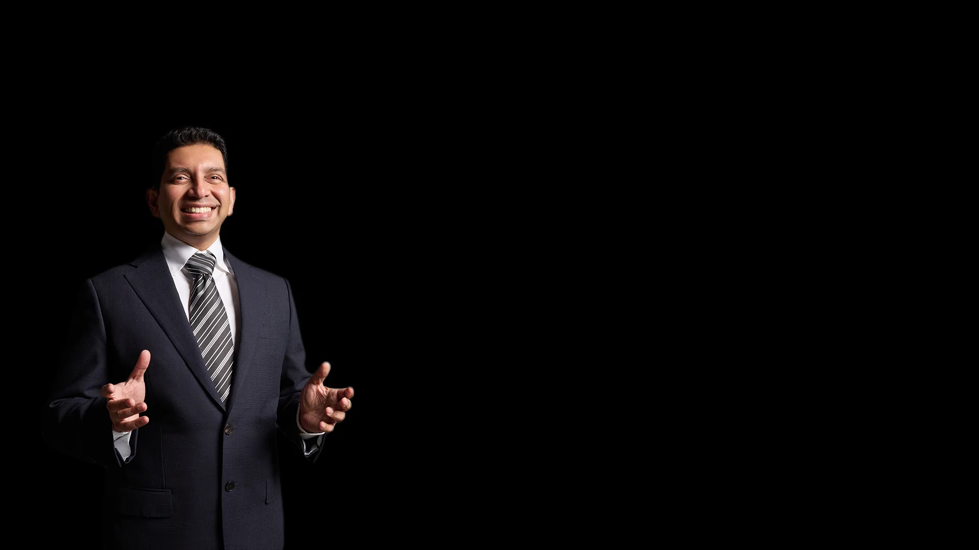 Dr Tiv, hands open mid-sentence, lit against a black studio backdrop